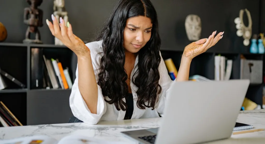 A woman at an office desk looks frustrated while working on her laptop. Modern office setting